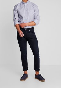 Vaaleansininen pitkähihainen nappipaita, yhdistetty tummansinisiin farkkuihin ja tummiin kenkiin. Paidassa on rintatasku ja hienovarainen tekstuuri.