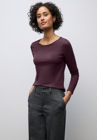 Long-sleeve, fitted top in deep purple cotton fabric, paired with gray plaid trousers featuring a button closure and side pockets.
