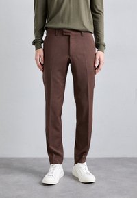 Braune maßgeschneiderte Hose aus leichtem Stoff, mit schmaler Passform, flachem Bund und dezenten Falten, kombiniert mit weißen Sneakers.