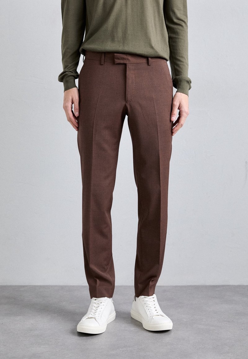 Braune maßgeschneiderte Hose aus leichtem Stoff, mit schmaler Passform, flachem Bund und dezenten Falten, kombiniert mit weißen Sneakers.