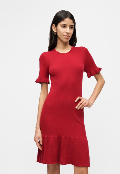 Κόκκινο πλεκτό φόρεμα με ριμπ ύφανση, κοντά μανίκια με βολάν και φαρδύ τελείωμα. Ομαλή υφή, εφαρμοστή σιλουέτα και στρογγυλή λαιμόκοψη.