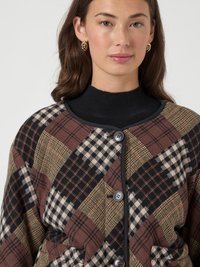 Brown and black plaid cardigan with geometric patterns, featuring a round neckline, button front, and two front pockets. Soft fabric texture.