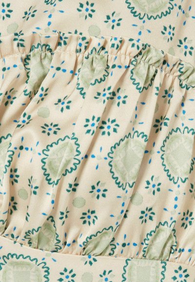 Tessuto color crema con sezione elastica arricciata caratterizzata da motivi floreali e puntinati verdi e blu in un motivo ripetuto.