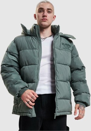 Puffer jacket in muted green, featuring a quilted design, high collar, and embroidered logo on the chest. Material appears smooth and shiny.