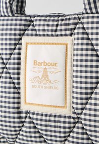 Καπιτονέ ύφασμα με μοτίβο καρό σε ναυτικό μπλε και άσπρο, που διαθέτει ένα κρεμ μπαλώμα με την ετικέτα "Barbour South Shields" και λογότυπο φάρου.