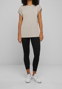 Lys beige kortærmet top, afslappet pasform, kombineret med sorte leggings og hvide sneakers. Glat stof, minimalistisk design, ingen synlige mønstre.