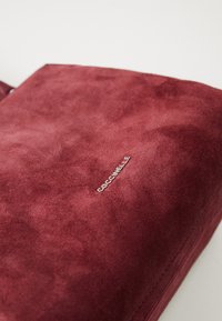 Burgundy suede bag featuring a silver logo detail, rectangular shape, soft texture, and clean lines with minimal hardware accents.