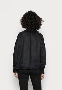 Svart blus gjord av texturerad tyg, med en rynkad halsringning och spetsdetaljer på ärmslut och fåll, med en avslappnad passform och lång ärm.