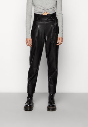 Schwarze Lederhose mit hohem Bund und Gürtel, kombiniert mit einem grauen, langen, gedrehten Crop-Top und schwarzen, schnürbaren Chunky Boots.