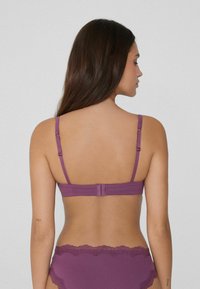 Fialová podprsenka se zapínáním na háček a očko na zadní straně, nastavitelnými ramínky a hladkou texturou. Minimalistický design bez vzorů.