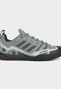 Γκρι και μαύρο ορειβατικό παπούτσι Adidas Terrex με κορδόνια, λαστιχένια προστατευτική μύτη, σχεδιασμένη πλευρά και θηλιά σε άσπρο φόντο.