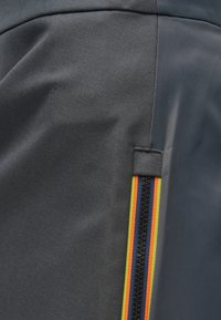 Tissu gris à texture lisse doté d'une fermeture éclair verticale soulignée par des bandes rouges, jaunes et bleues. Le design met en avant un style moderne.