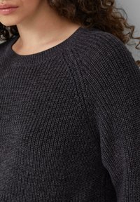 Dunkelgrauer Strickpullover mit geripptem Muster, rundem Ausschnitt und Raglanärmeln. Nahaufnahme zeigt die Stoffdetails und Nähte.