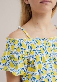 Off-the-shoulder topp med tryck av gula citroner och blå blad, tillverkad av lätt bomullstyg, med elastisk smockdetalj vid halsringningen.