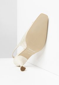 Scarpa con tacco in patent pelle avorio, con punta affusolata e tacco sottile, caratterizzata da una suola testurizzata e un design con ritagli laterali. Taglia 37.