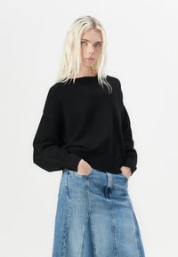 Czarny dzianinowy sweter o luźnym kroju, okrągłym dekolcie i długich rękawach, w połączeniu z niebieską max spódnicą z denimu z detalami szwów.