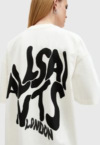 Biele bavlnené tričko s oversized čiernou typografiou na chrbte. Má voľný strih, krátke rukávy a okrúhly výstrih.