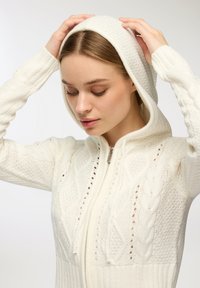 Biała dzianinowa bluza z kapturem z zamkiem błyskawicznym, posiadająca fakturowane wzory w warkocze oraz dopasowany krój z miękką podszewką.