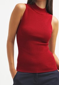 Rood geribd mouwloos topje met een hoge hals, voorzien van een aansluitend ontwerp en een gestructureerde stof. Geen extra versieringen of patronen.
