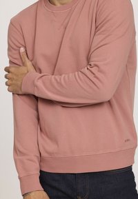 Sweat-shirt en coton rose avec des poignets et un ourlet côtelés, doté d'un col rond et d'un détail de logo discret sur le côté inférieur.