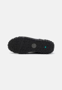 Black rubber sole with rugged, multidirectional tread pattern. Features a circular logo and a turquoise accent near the heel.