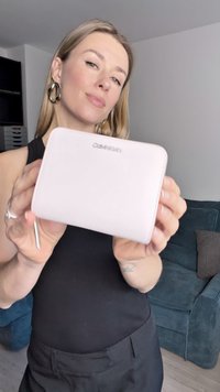 Portafoglio in pelle rosa con una texture liscia, bordi arrotondati e logo in rilievo sul davanti. Presenta una cerniera argentata e sottili dettagli di cucitura.