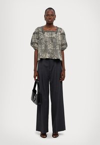 Svart og kremmønstrete cropped bluse med puffärmer, kombinert med høytlivede mørkegrå vide bukser og svarte tilbehør.
