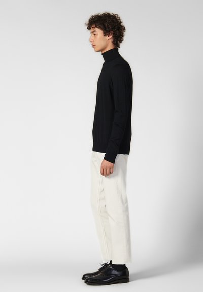 Maglione a collo alto nero realizzato in tessuto morbido, design aderente con polsi a costine, abbinato a pantaloni bianchi a sigaretta e scarpe nere eleganti.