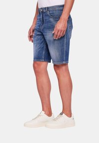Shorts in denim di un blu medio, con un classico design a cinque tasche, taglio dritto e cuciture a contrasto, abbinati a sneakers bianche.
