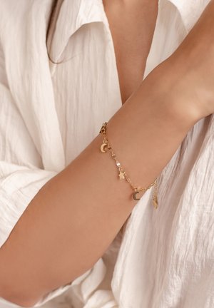Goldene Kettenarmband mit Halbmond- und Sternanhängern. Leichtes Design mit einer zarten, glänzenden Textur vor einem hellen Hintergrund.