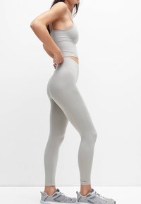 Leggings de sport gris clair avec une taille haute et une texture lisse, accompagnés d'un débardeur court assorti. Présente des détails de couture subtils.