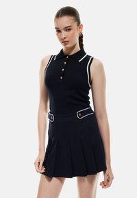 Polo sans manches bleu marine avec des bordures blanches, doté d'une patte de boutonnage et d'une coupe ajustée, associé à une jupe plissée avec des boutons décoratifs.