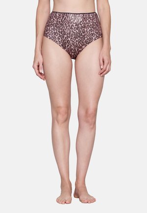 Frau trägt hoch geschnittene Slips mit pink-braunem Leopardenmuster, steht barfuß vor einem schlichten hellen Hintergrund.