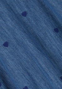 Tissu en denim bleu présentant de petits motifs de cœurs navy éparpillés sur la surface, avec une finition texturée et une légère variation de couleur.