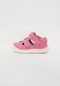 Roze suède cipele s dva prilagodljiva Velcro remena i bijelim gumeni potplat. Sa strane se nalazi brend logo u reljefnom kružnom dizajnu.