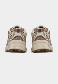 Ζευγάρι αθλητικών παπουτσιών σε μπεζ και καφέ αποχρώσεις, με την πίσω πλευρά να φαίνεται, και με υφή στις σόλες και λεπτομέρειες από δίχτυ, σε απλό φόντο.