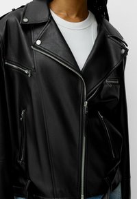 Černá koženka bikerská bunda s stříbrnými zipy, s klopovým límcem a několika kapsami na zip. Texturovaný povrch a strukturovaný design.