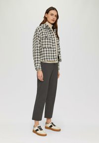 Veste à motif pied-de-poule noire et blanche, associée à un pull crème et un pantalon gris. Les chaussures présentent des accents beige et noir.
