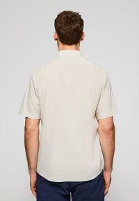 Lichtbeige kortemouwhemd met een rechte snit, zachte textuur en een klassieke kraag. Heeft een effen ontwerp zonder zichtbare patronen.