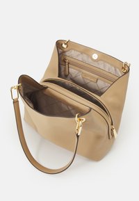 Sac à main en cuir tan au design structuré, avec des accessoires en métal doré. L'intérieur comprend une poche zippée et un revêtement en tissu beige matelassé.