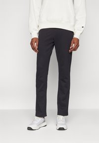 Pantalones oscuros de color gris con un corte ajustado, hechos de una tela suave. Combinados con una sudadera blanca con capucha y zapatillas deportivas ligeras de color gris. Diseño minimalista, sin patrones.