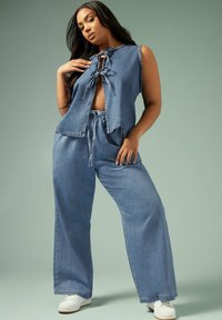 Ljusblå denim tvådelat set som består av en ärmlös topp med knytfram och vida byxor, med en mjuk textur och avslappnad design.