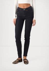 Jeans de tiro alto azul oscuro con cinco bolsillos, costuras naranjas, ajuste slim y combinados con unos zapatos planos de estampado animal marrón con tiras negras.