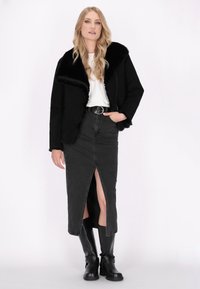 Veste en shearling noire avec un large col, associée à une jupe en denim noir à fente haute et des bottes noires jusqu'aux genoux. Top blanc simple en dessous.
