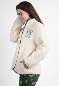Chaqueta de forro polar color crema con cuello alzado, con ribete verde y un gráfico frontal de un personaje con el texto "LA FUERZA ES FUERTE."