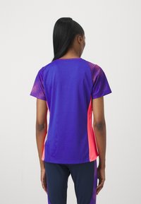 Top atlético con una mezcla de tonos púrpura y rosa, mangas cortas y un patrón texturizado en los hombros, hecho de una tela ligera.