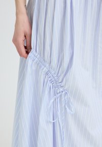 Main tenant un tissu rayé bleu clair et blanc rassemblé avec un cordon noué sur une jupe ou une robe.