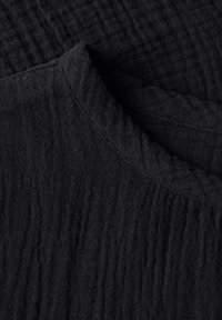 Tissu noir texturé avec une apparence froissée et un col rond. Le matériau est doux et léger, adapté à une tenue décontractée.