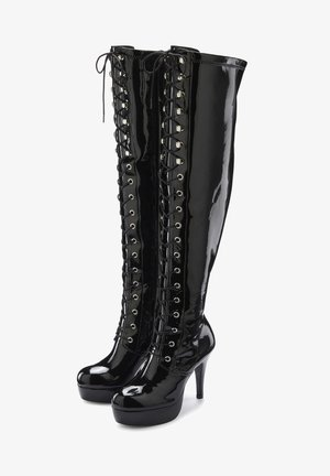 Stiefel mit hohen Absätzen aus glänzendem schwarzem Lackleder, die bis zum Oberschenkel reichen, mit Schnürung vorne und silbernen Ösen, ausgestattet mit einer Plattformsohle für zusätzliche Höhe.