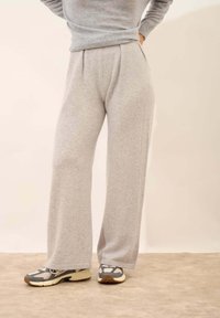 Šedé široké tepláky vyrobené z měkkého materiálu, s plisovaným předním dílem, spárované se šedými a bílými teniskami. Hladká textura.